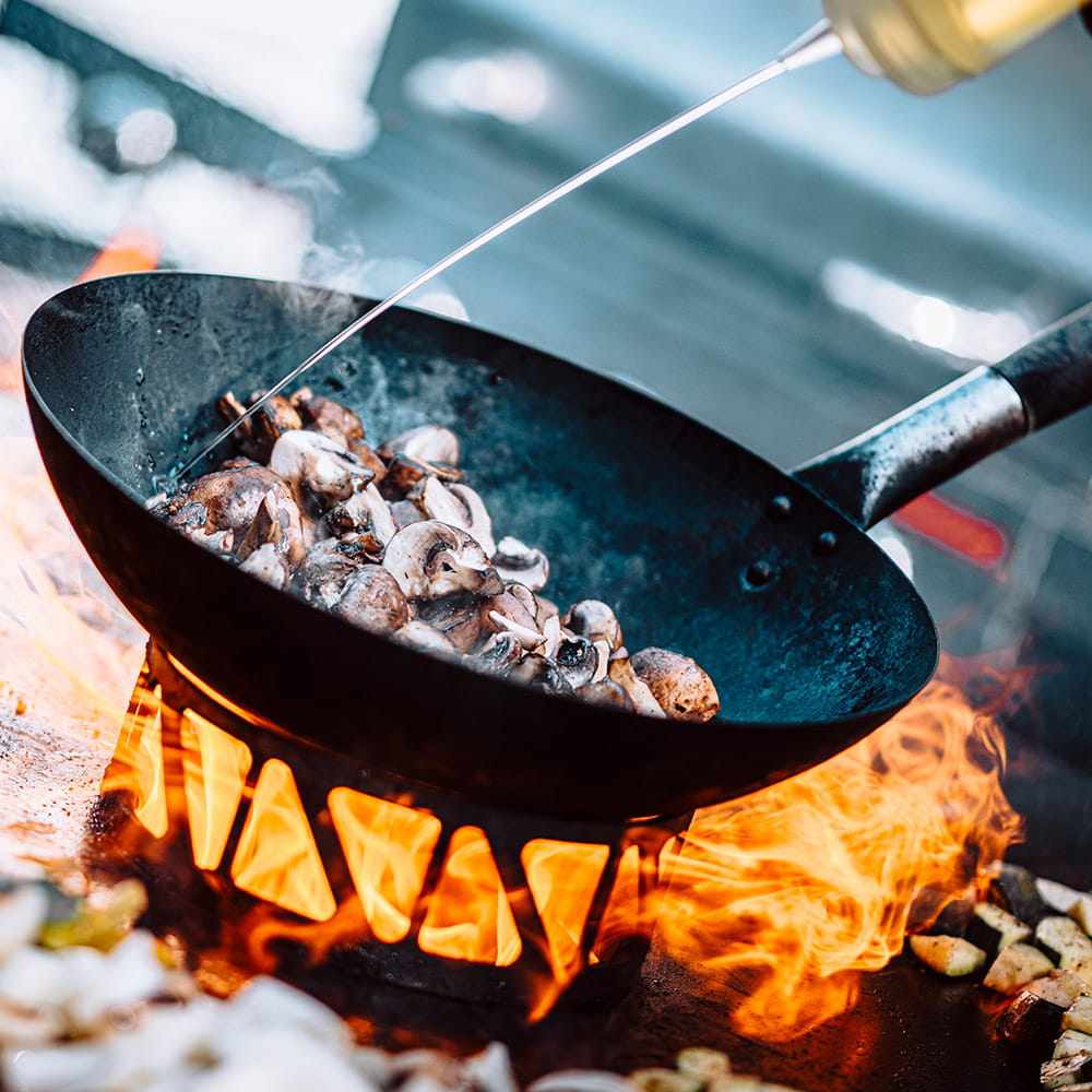 Champignons werden in einer Pfanne über offenem Feuer gebraten